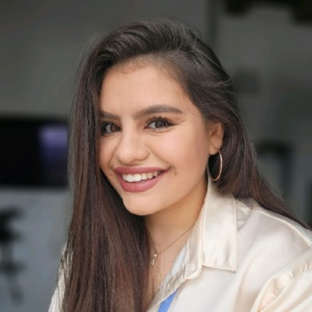 Woman with long dark hair and hoop earrings, smiling at the camera indoors.